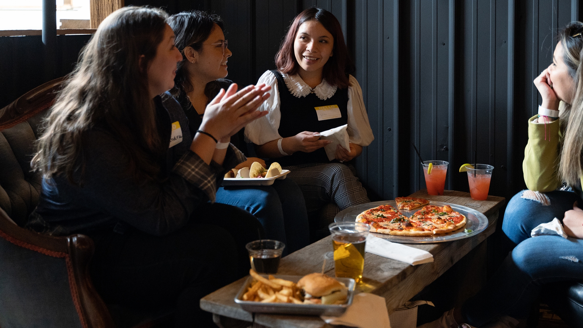 A group of people sitting together talking and eating pizza