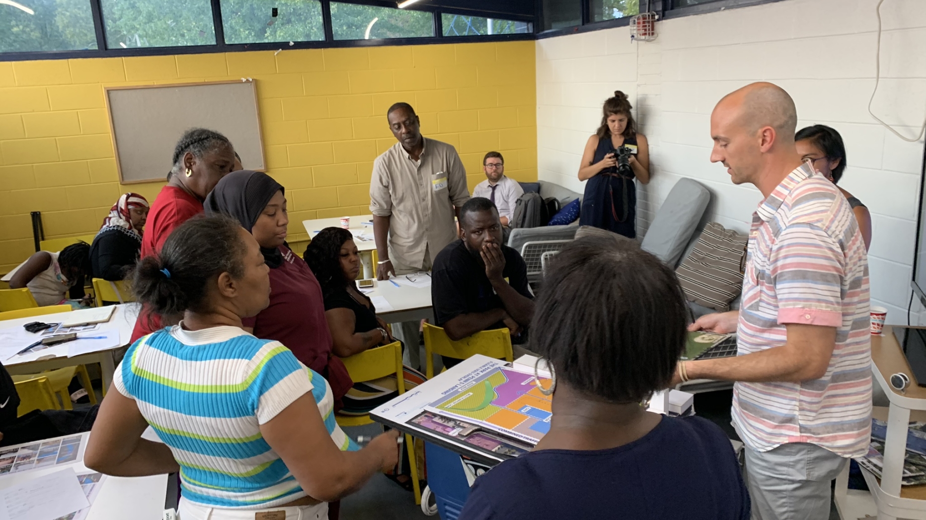 Man giving presentation while people stand with him around a table listening