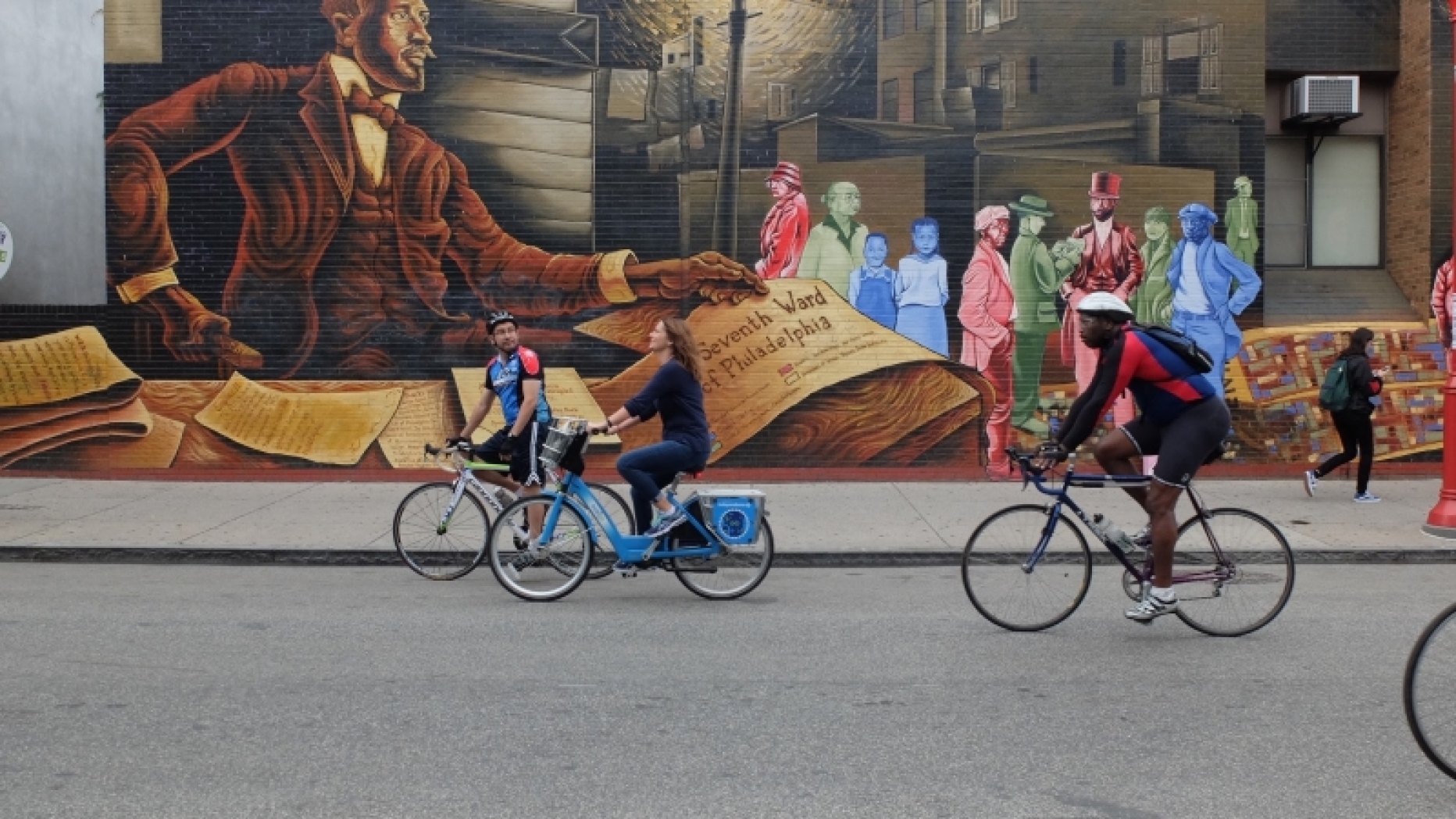People riding bicycles in front of a mural.