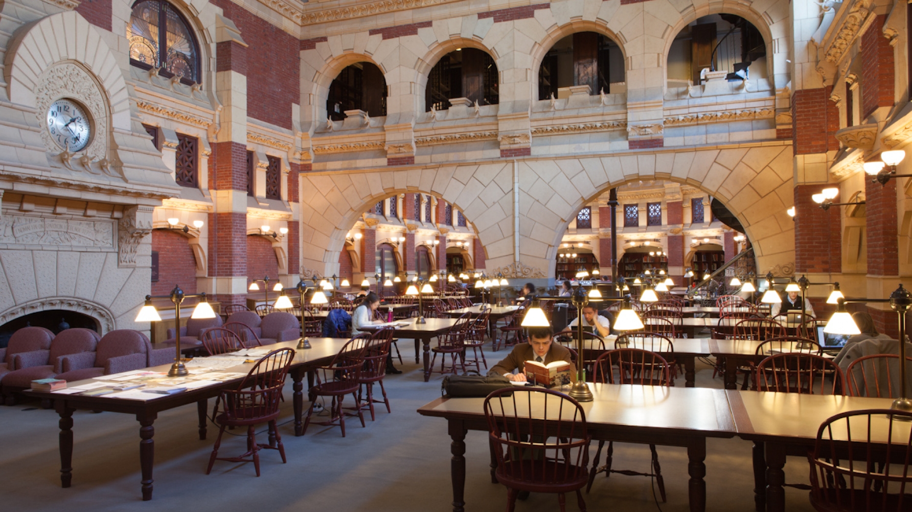 Huge library space with stone arched architecture and several students working at large wooden tables