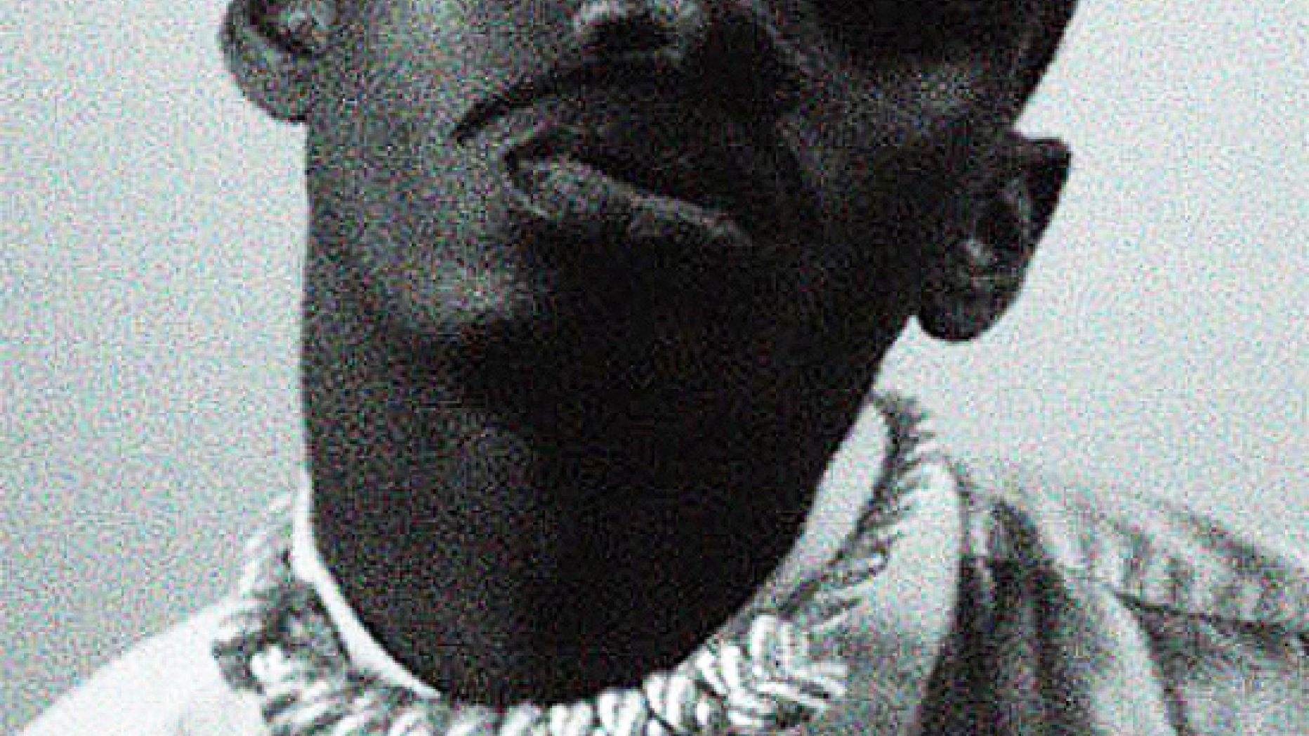 Photograph of a young black man wearing a necklace that stylistically resemble a noose.