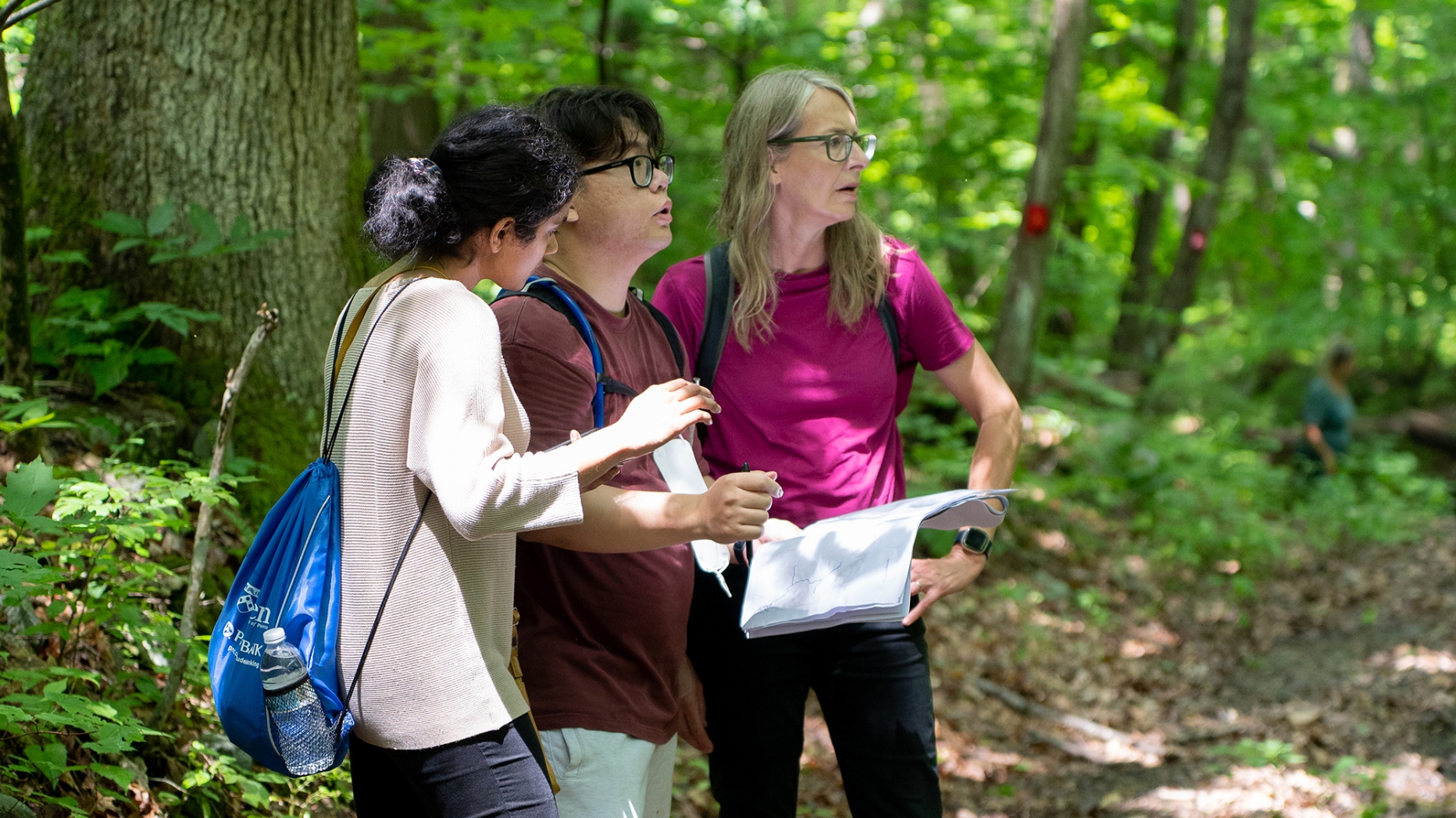 Three people refer to a map standing in the woods