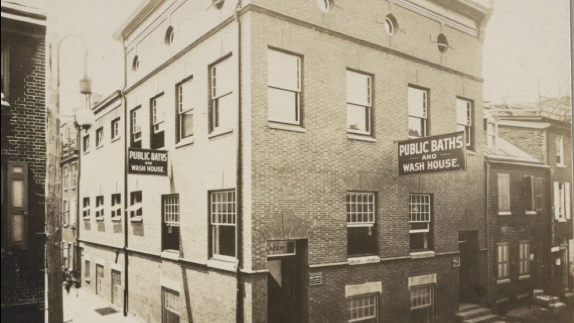 Black and white photo of a building with a sign: Public Baths and Wash House