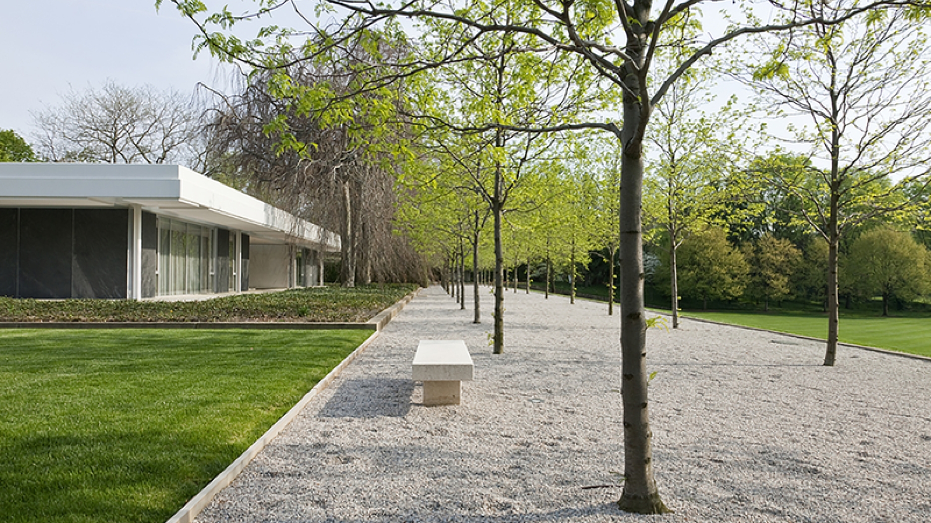 A modernist house with a gravel walkway and bench in front