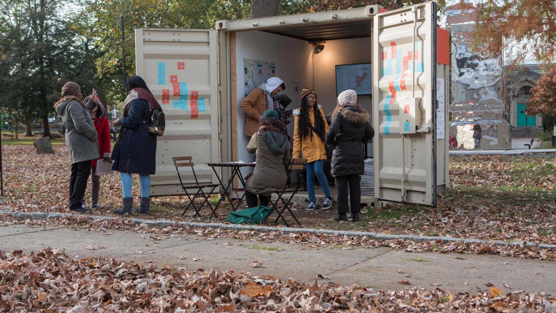 Students holding an information booth in a small cargo container during fall
