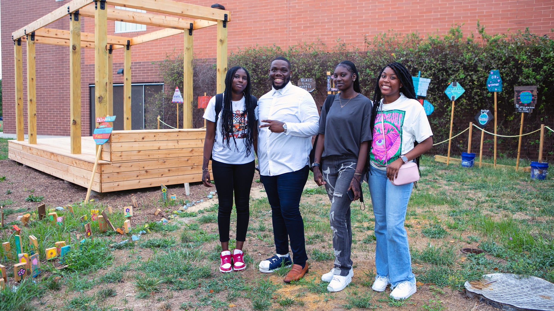 Four students pose beside a wooden structure