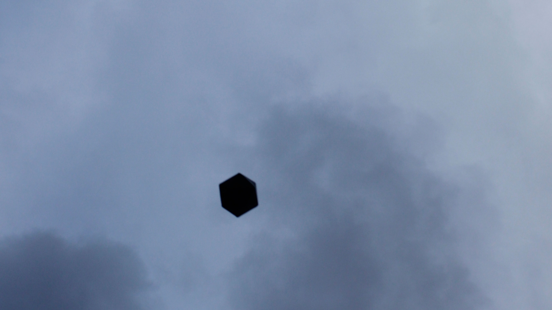Image of clouded sky with a black hexagon in the middle.