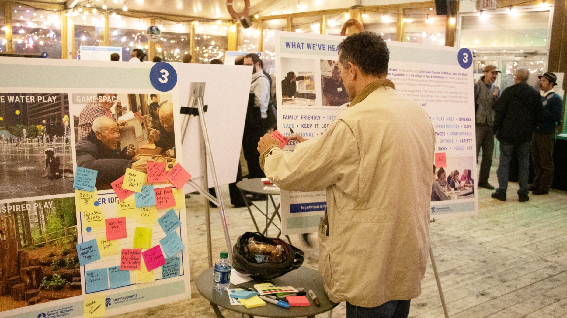 Man putting sticky notes on a poster board in a large conference space