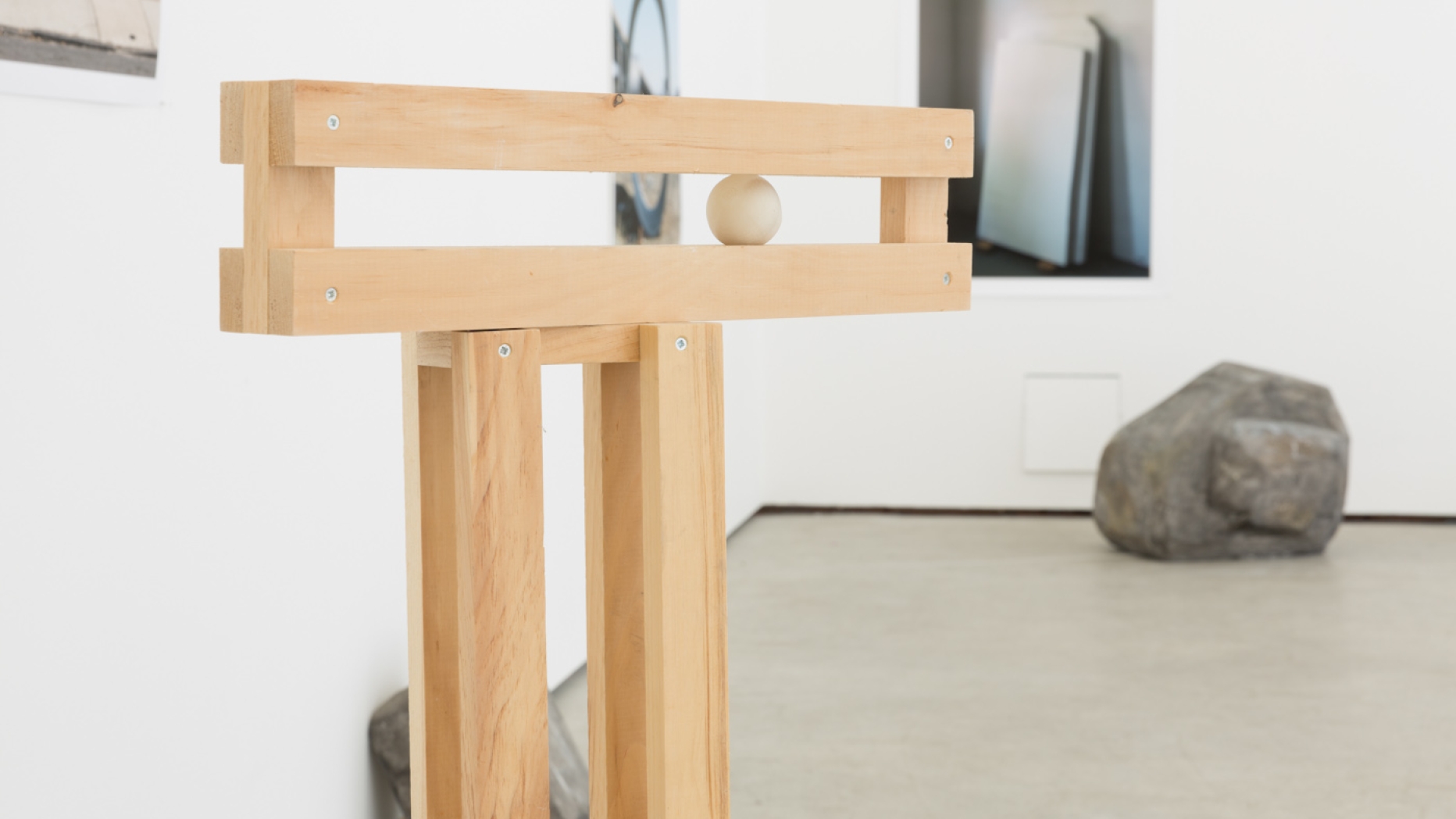 Sculpture featuring rectangular wooden planks holding a small wooden ball.