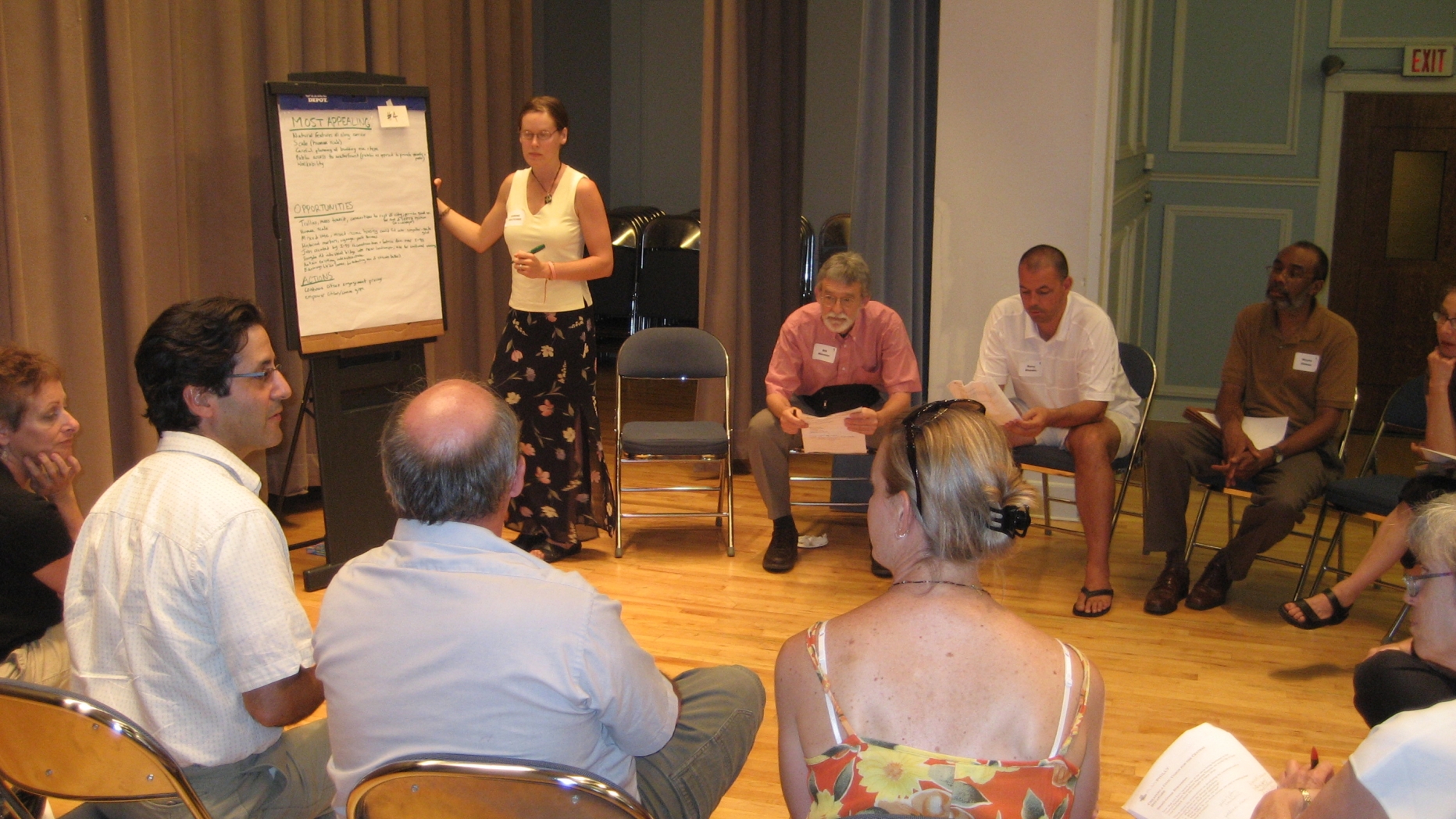 Project participants sit in a circle of chairs and discuss issues written on a large pad of paper at the front of the room.