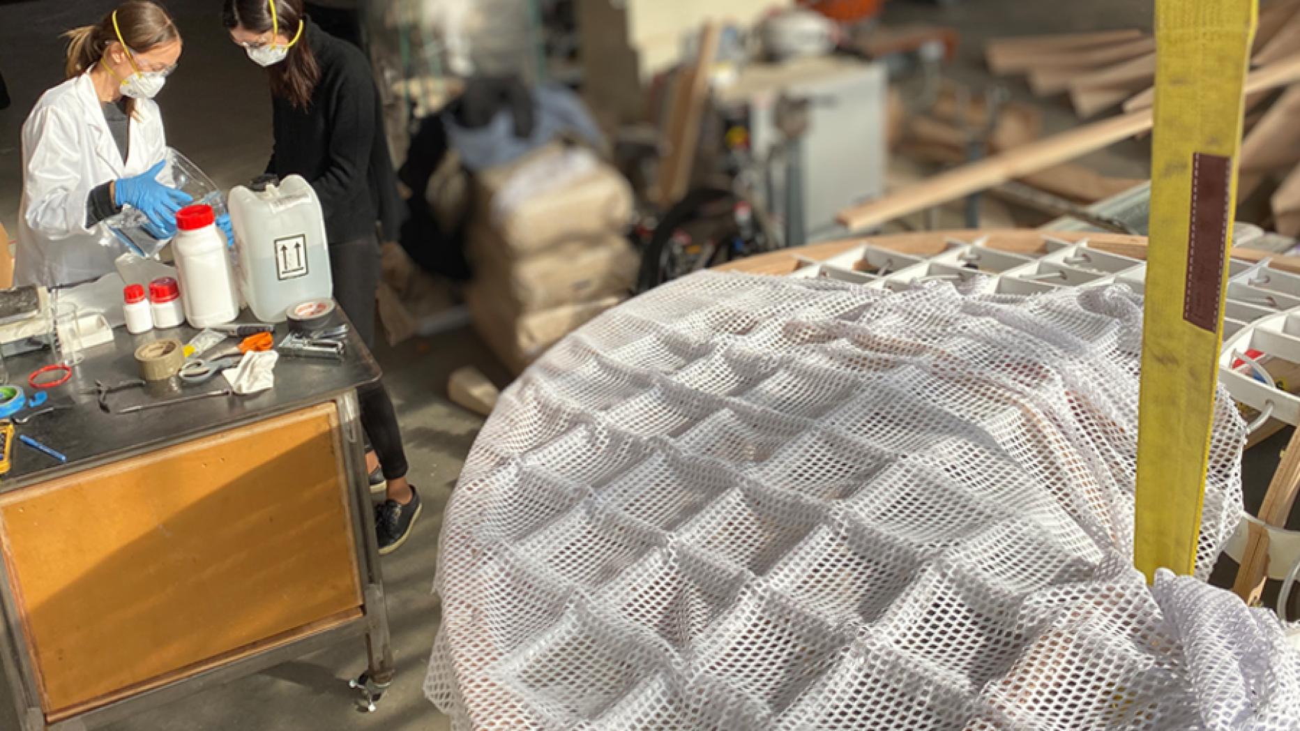 two women stand next to saucer-like honeycomb structure in industrial lab