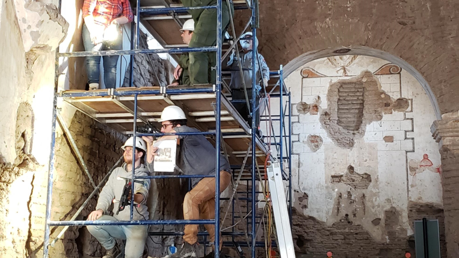 Group of students on scaffolding within large run down room doing restoration work