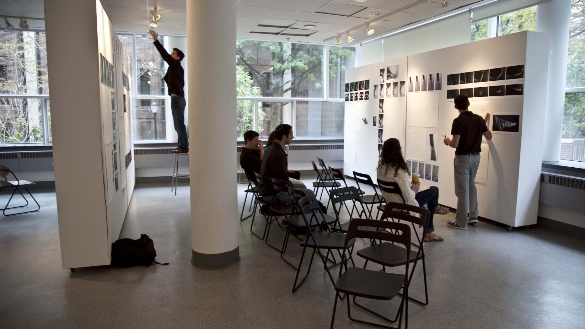 Student giving presentation in openly structured studio space. Opposite him is another student adjusting rack lighting