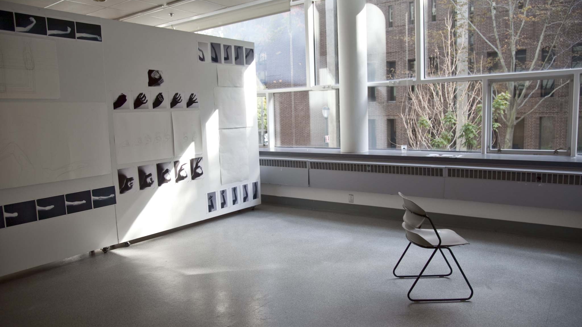 Sunlit, unoccupied studio space with photos displayed on wall and empty chair.