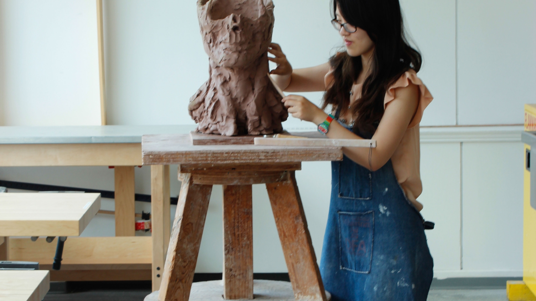 Student working clay in to a form that resembles the lower half of a human head and neck.