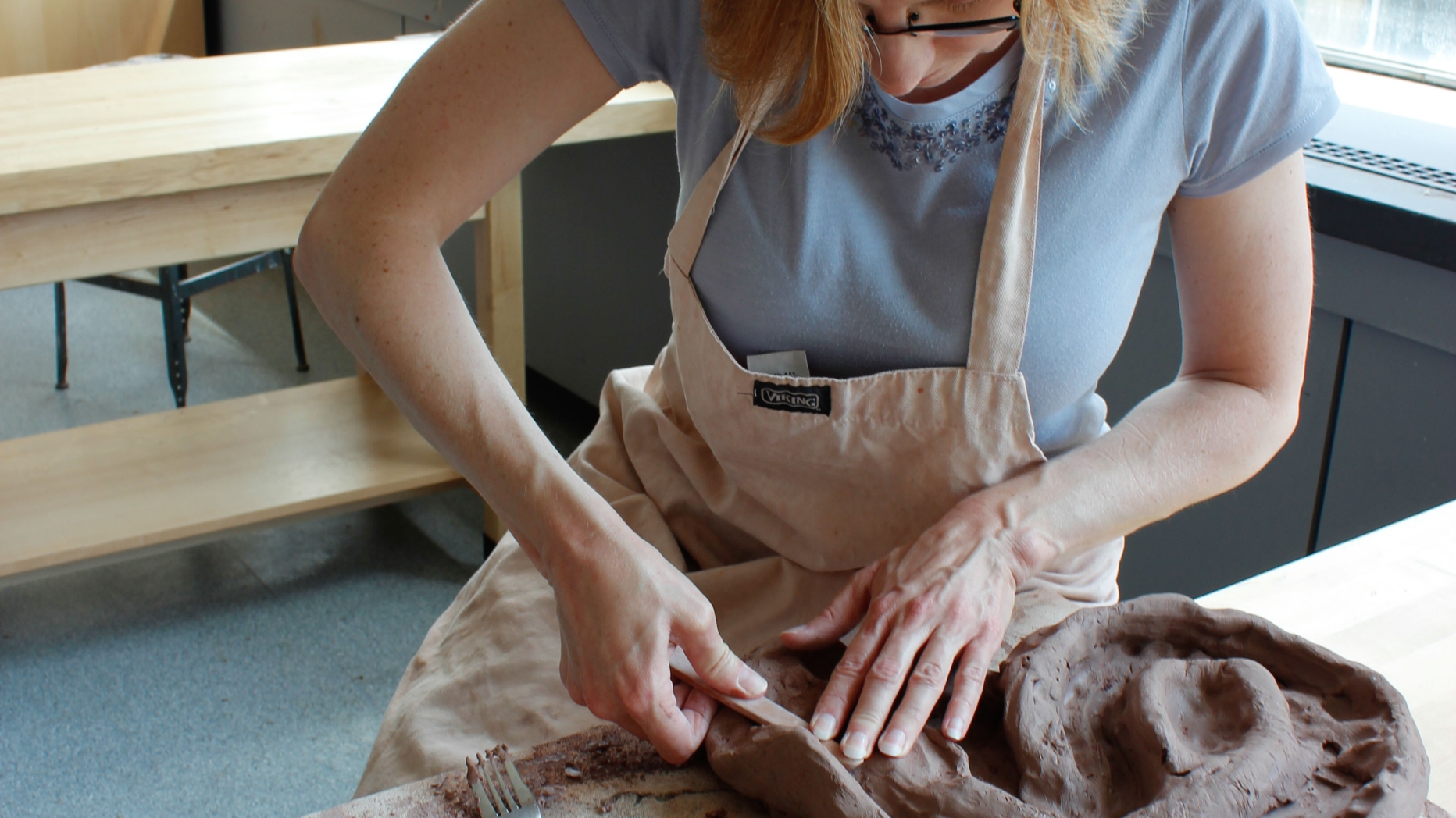 Student sitting in sunlit studio molding clay in to a spiral pattern.