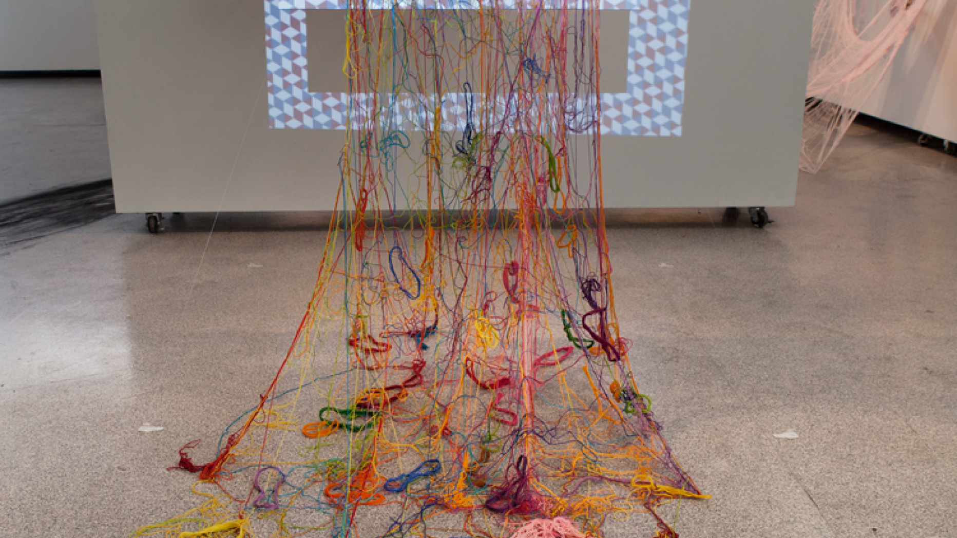 Art piece featuring pieces of yarn connected to a board being spread out in a messy fashion across the floor