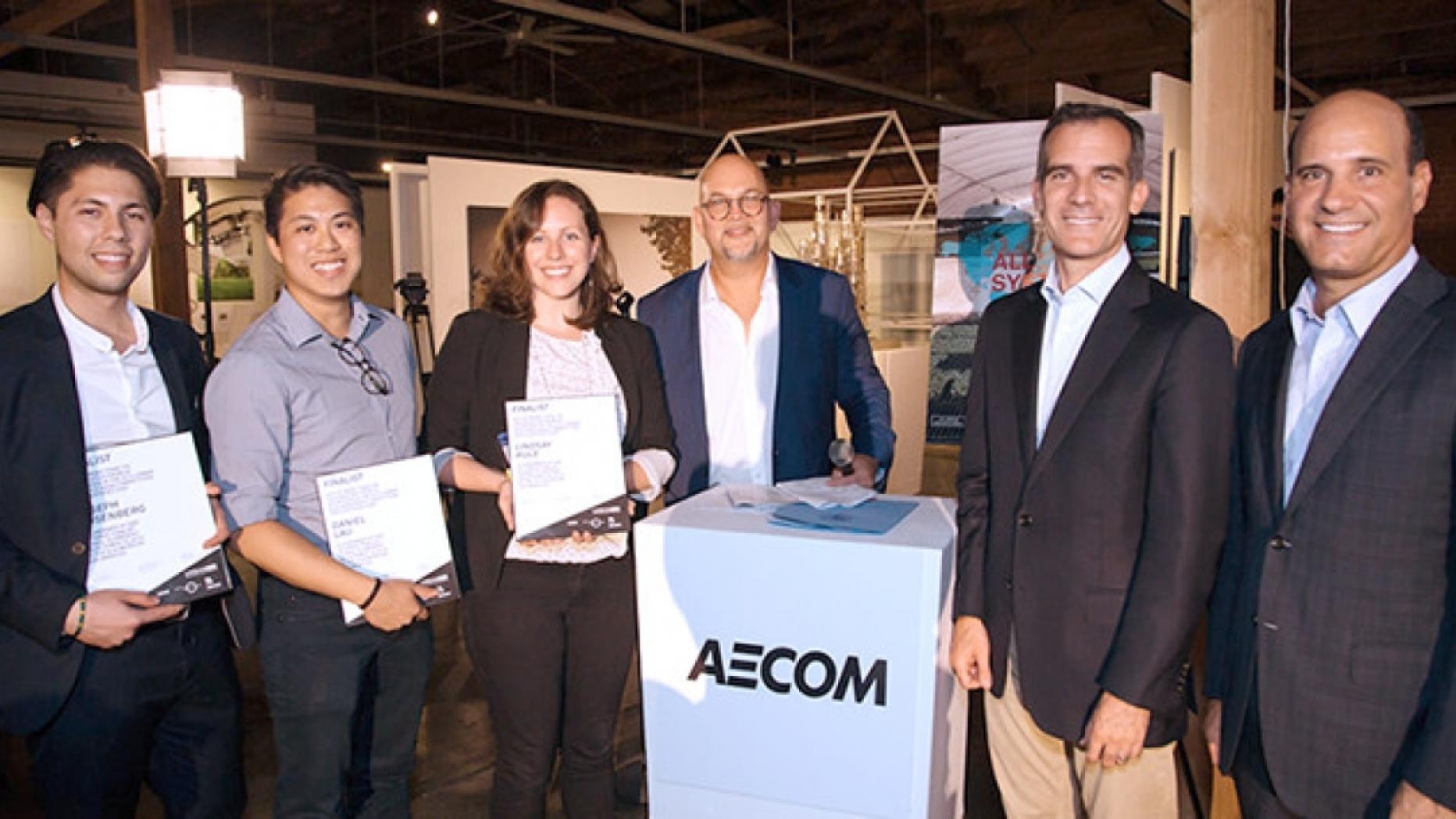 A group of six people pose next to a pedestal with the word AECOM on it