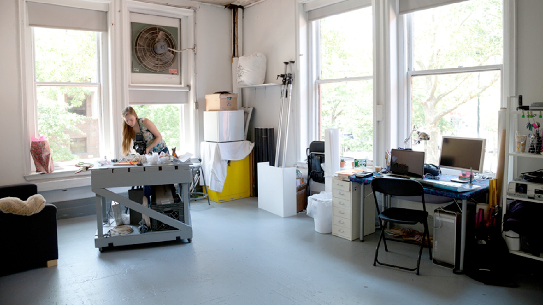 In a large studio space with large windows a student works at a work table in the middle of the room