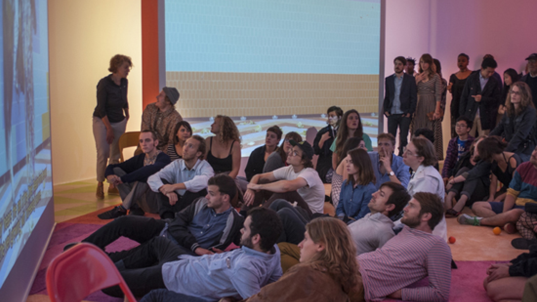 Students lying on the ground in a room looking at a projected presentation on the wall.