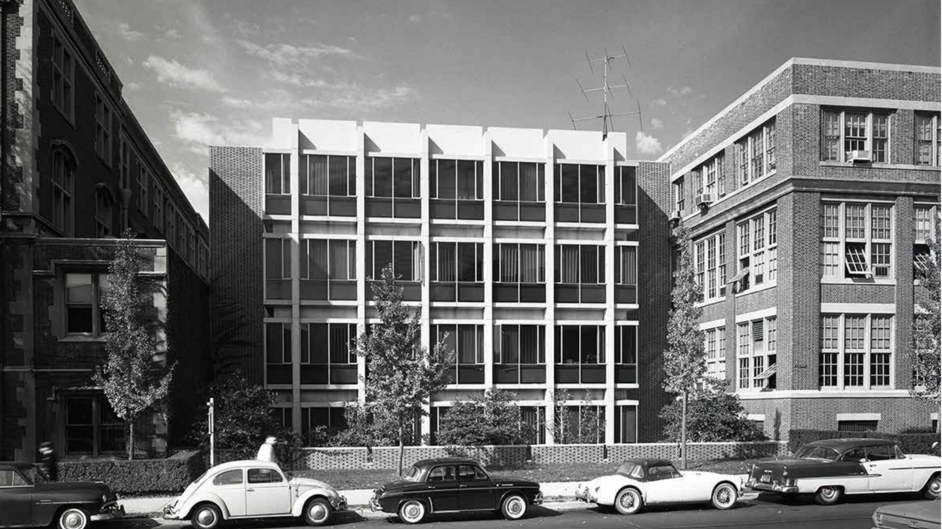 black and white photo of modernist building with old cars parked on street