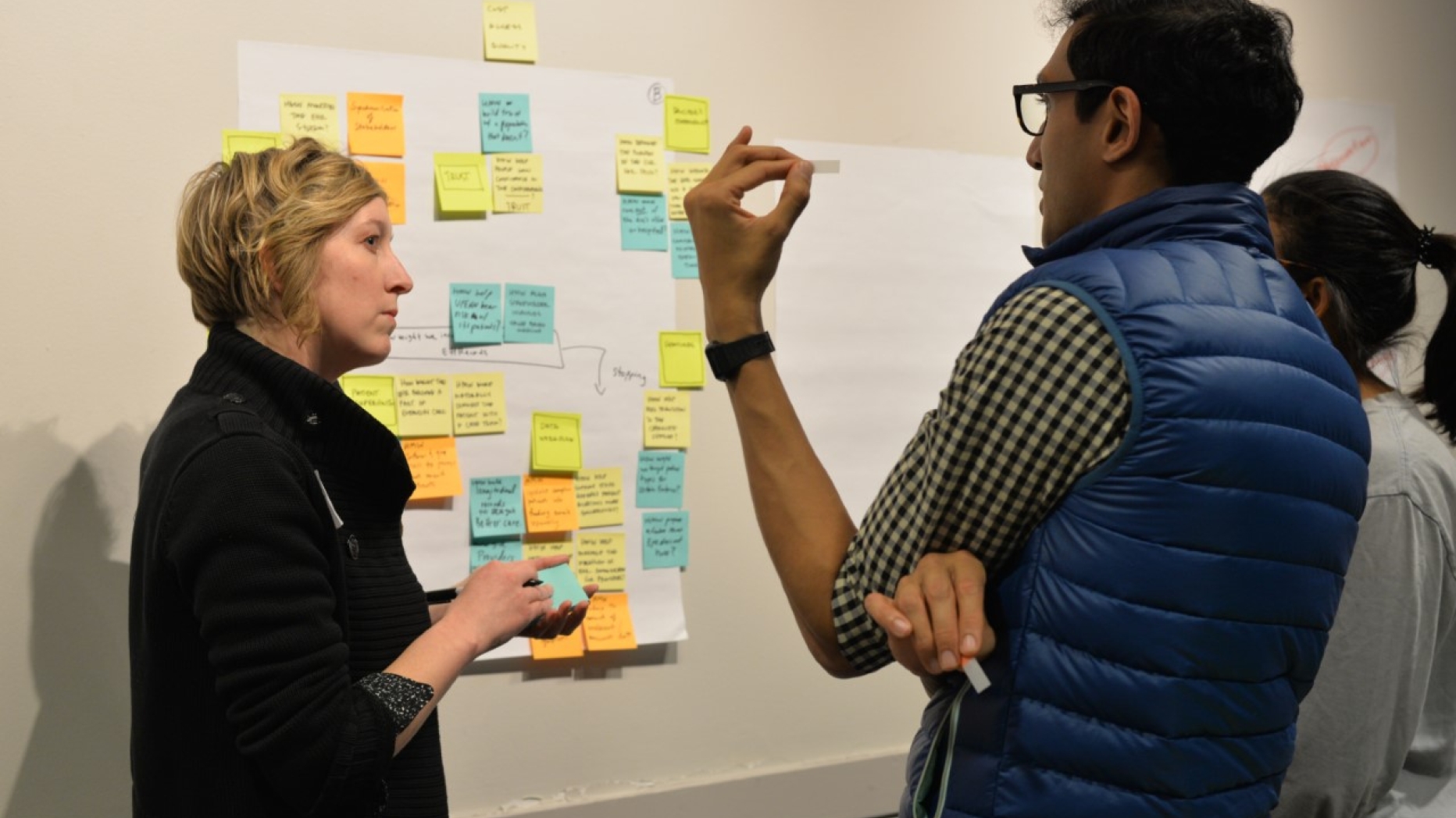 People talking next to a poster board with sticky notes all over it