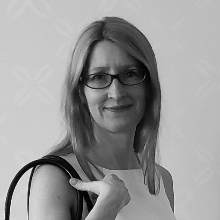 a black and white image of Karen M'closkey wearing small square framed galsses smiling over her right sholder toward the camera 