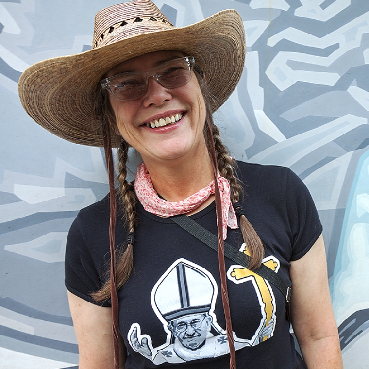 Rodewald is pictured against a colorful mural backdrop and wears a hat and black t-shirt