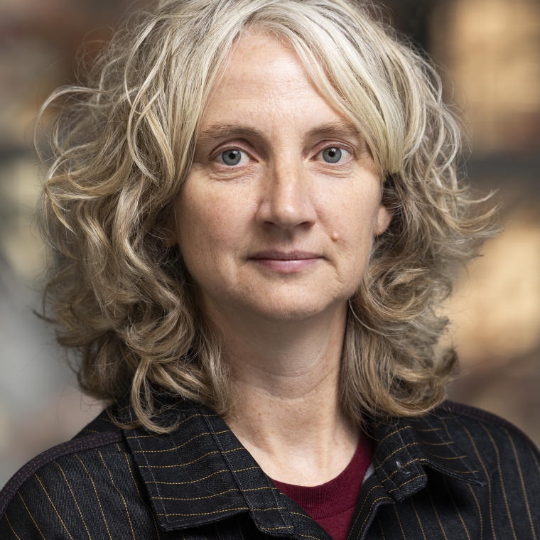 Tight cropped portrait of middle aged white woman with shoulder length, curly gray and brown hair.