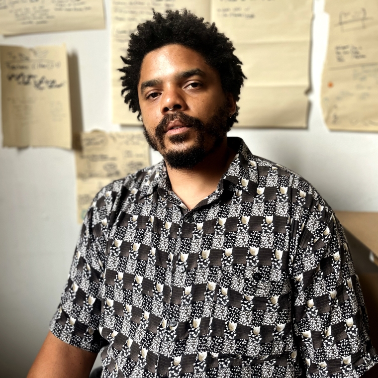 Photo of fields Harrington sitting in front of a white wall with papers tacked on it behind him