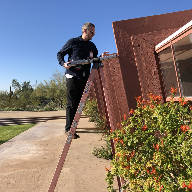 person measuring architectural wood on ladder