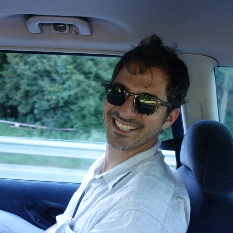 Photograph of Joshua Simon sitting in a car wearing sunglasses and a white shirt