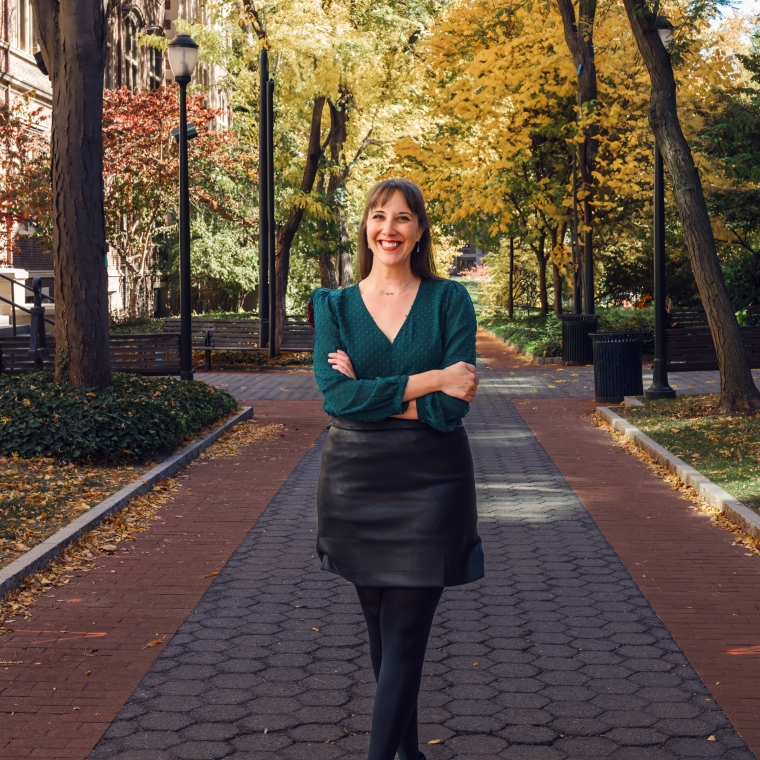 Photograph of a woman with brown hair standing on a paved path