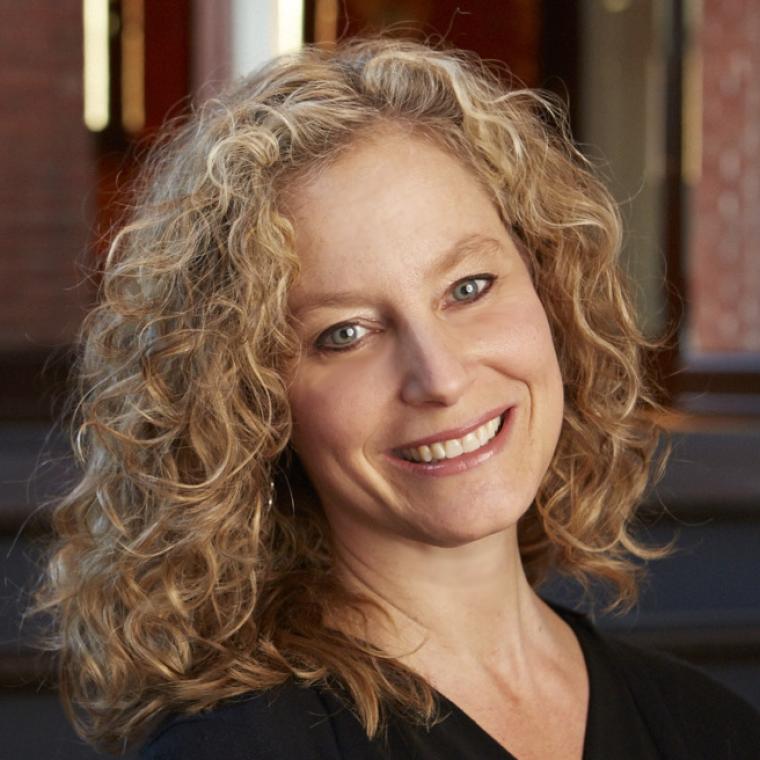  Headshot of head and shoulders with smiling face, curly blonde hair, head tilted to left