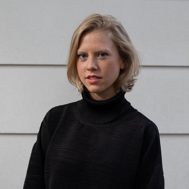 Lerner looks at camera, shoulder-length blonde hair and wears a black turtleneck shirt