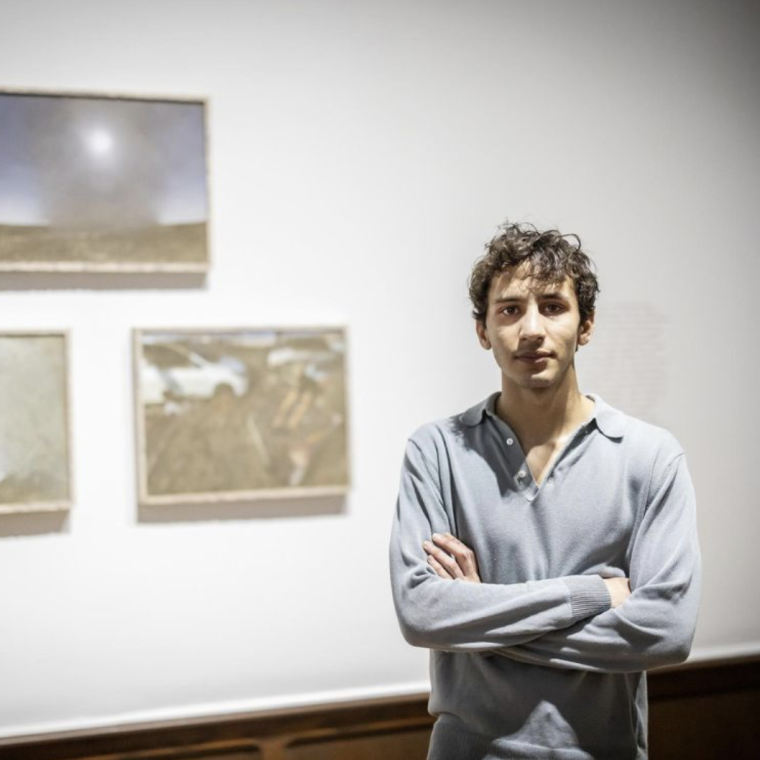 Photograph of Eissa Attar standing in front of 3 of his prints in the exhibition.