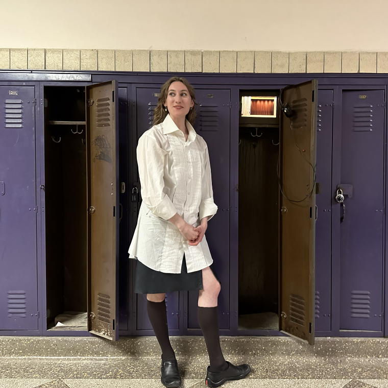 Photograph of Susannah Ogler standing in front of a wall with purple lockers, smiling and looking off to the side