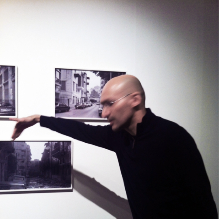 Photograph of Walid Road in motion, gesturing to one of three black and white photographs hung on a white wall