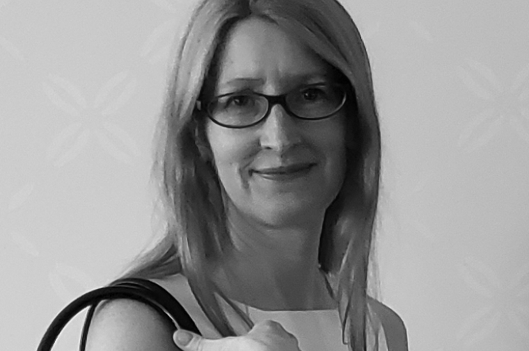a black and white image of Karen M'closkey wearing small square framed galsses smiling over her right sholder toward the camera 