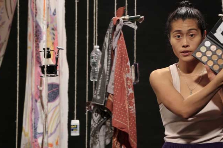 Young Asian woman with household items suspended next to her displays a makeup kit