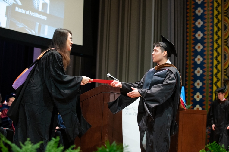 A robed grad accepts diploma from robed faculty member on stage