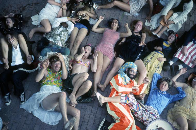 lots of people in strange clothing lying on floor smiling at the camera above them