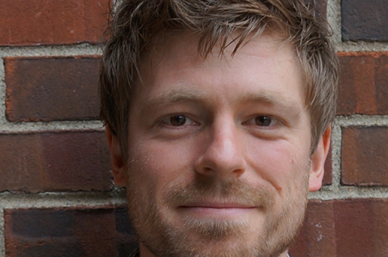 Nicholas Pevzner against red brick wall background, looking into camera