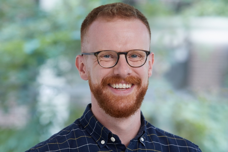 image of a man with red hair, thin framed glasses smiling in a dark blue button down shirt