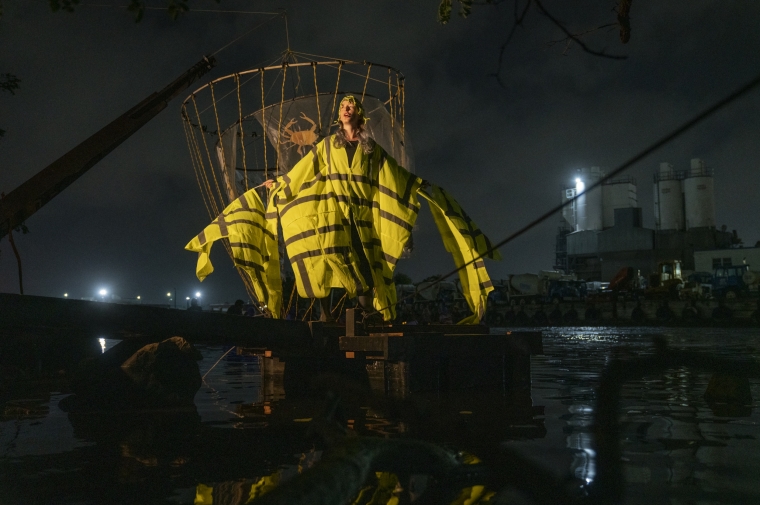 a photo of a person in a yellow and black detailed dress floating above an audience in front of a dark night and river backdrop