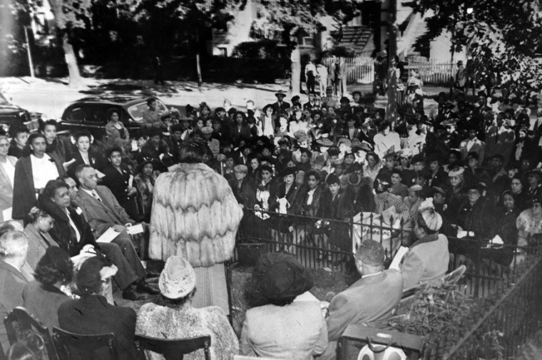 black and white photo of a crowd facing figure in fur coat