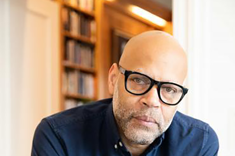 Photograph of Kevin Jerome Everson leaning on a counter in front of bookshelves