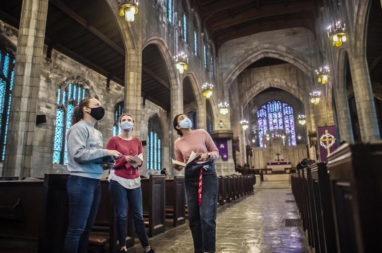 Three students looking up in the center aisle of a cathedral.