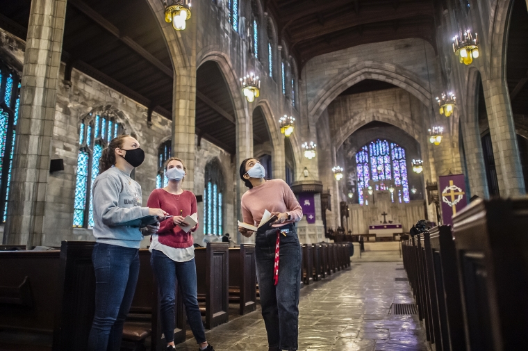 Three students looking up in the center aisle of a cathedral.