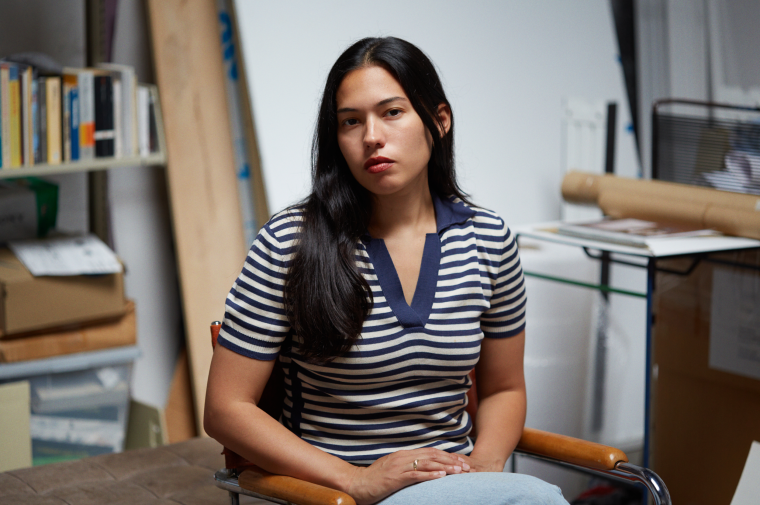 Photograph of Rose Salane sitting in her studio in front of a bookshelf 